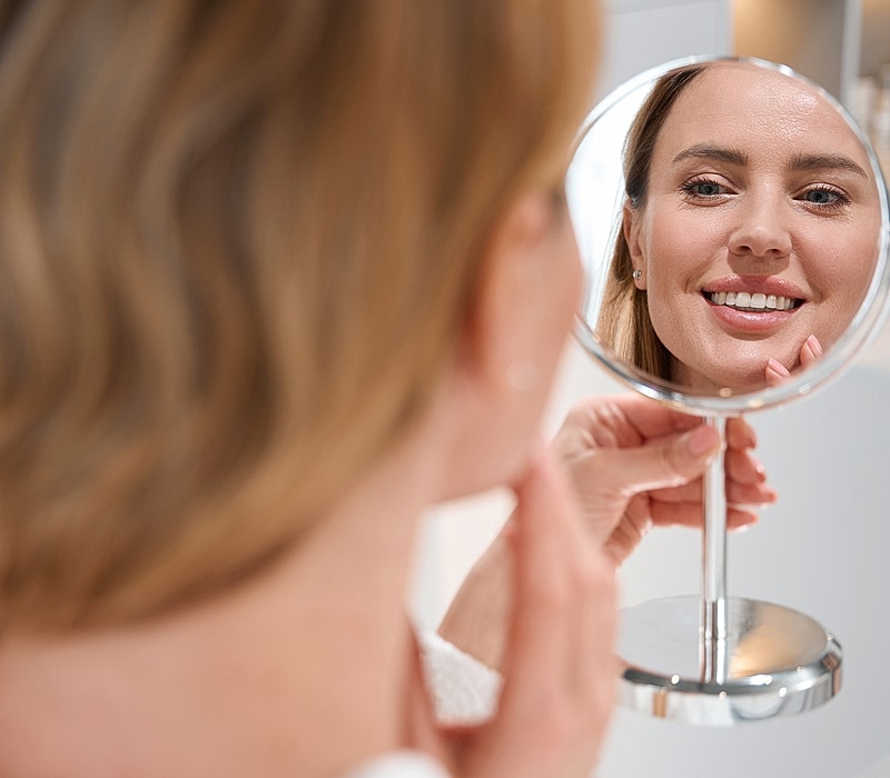 Woman admiring reflection in a handheld mirror.