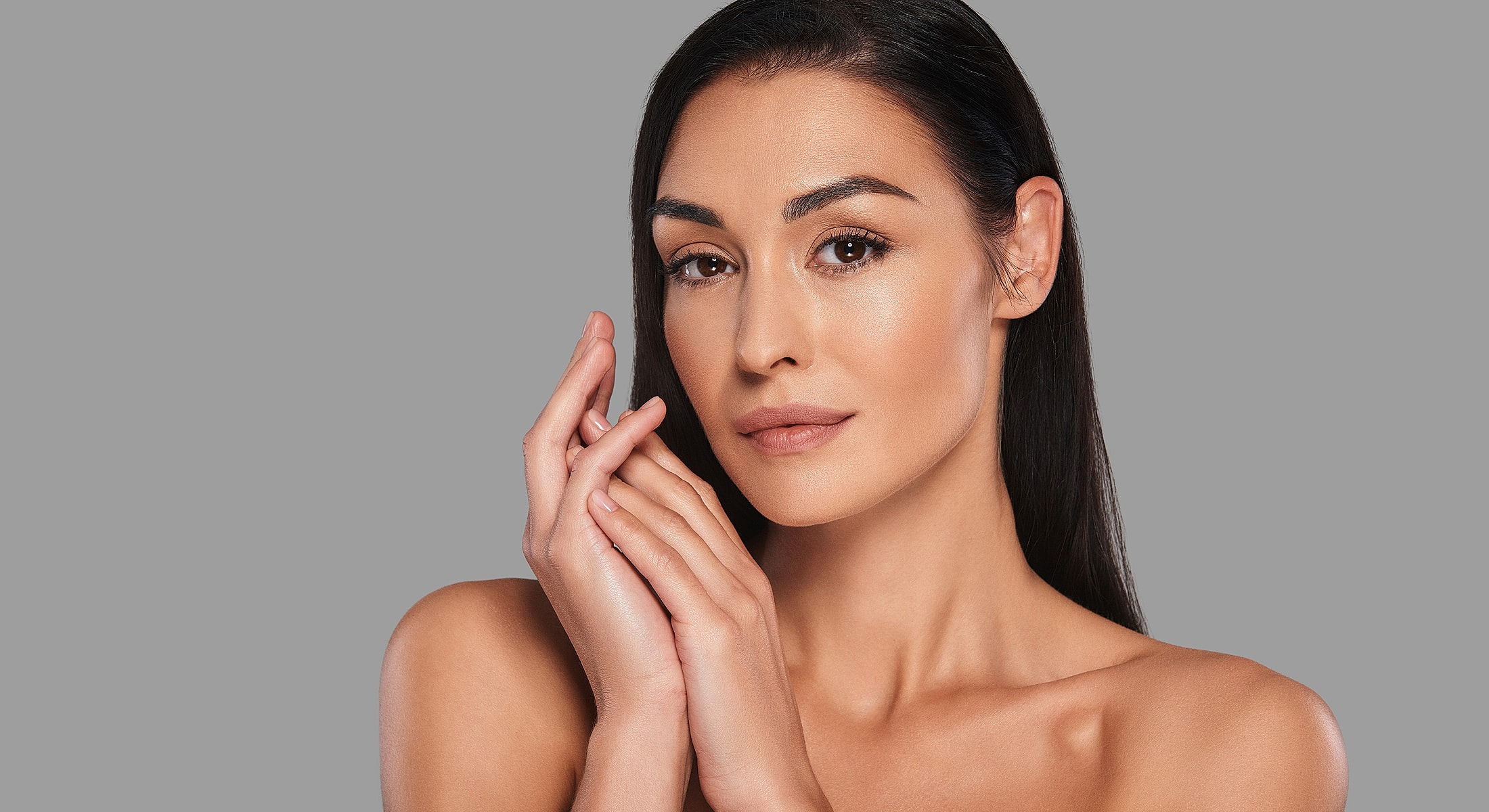Woman with long hair posing elegantly, neutral background.