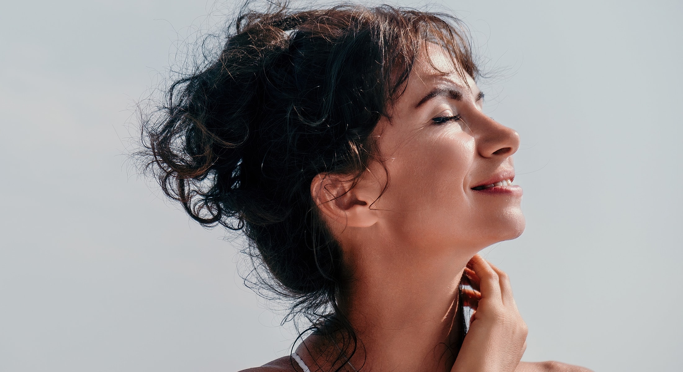 Woman smiling with curly hair against sky.
